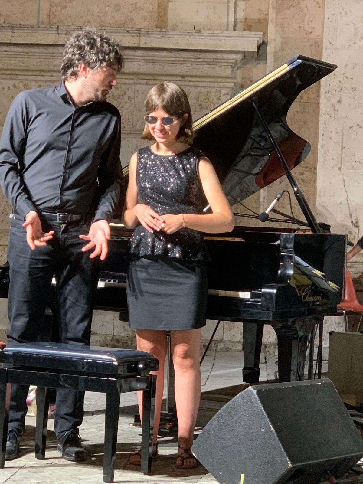 Anna sorridente accanto al gran coda, con un musicista